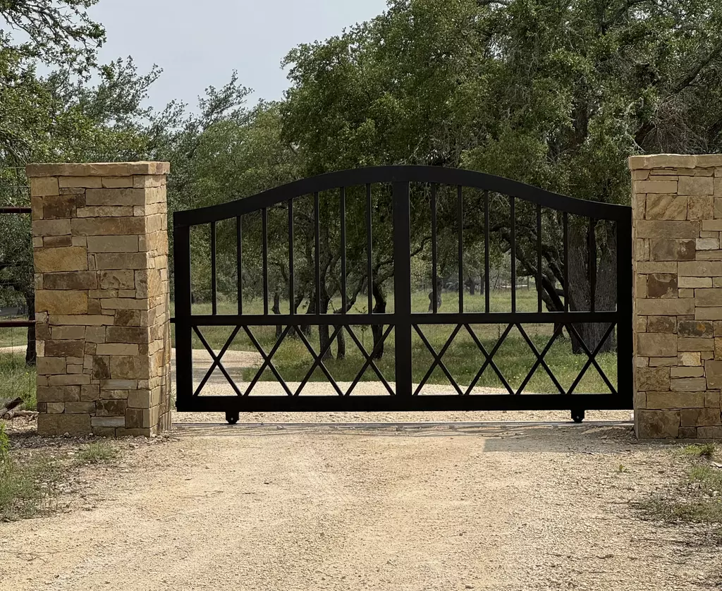 Black metal bell arched swing gate with two stone pillars in brown stone
