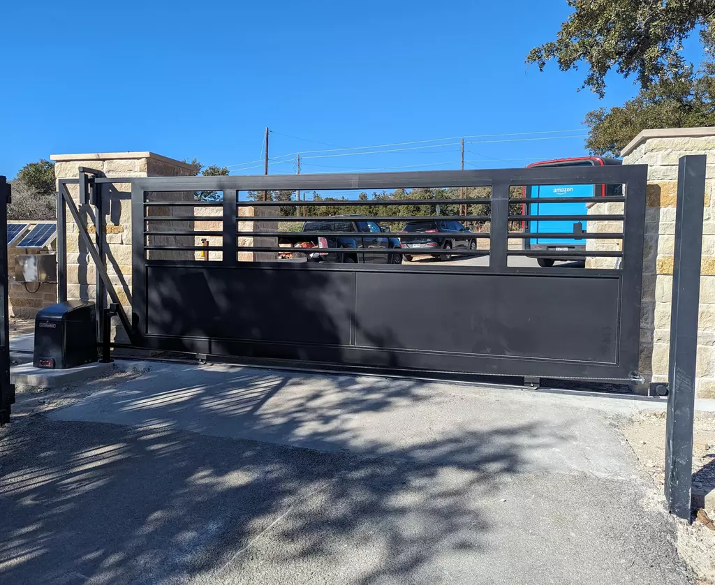 Modern metal dark gray gate that slides on a track to open. Solid bottom half with bars on top half with a flat top.