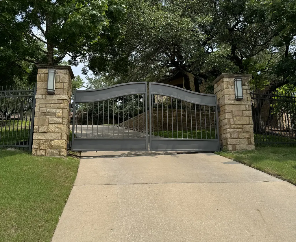 Gray Metal bell arched swing gate with beige stone pillars on either side
